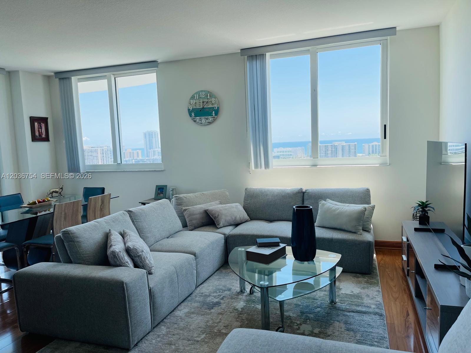 A living room with a gray sectional sofa, glass coffee table, and ocean view windows — HALLANDALE BEACH, FL