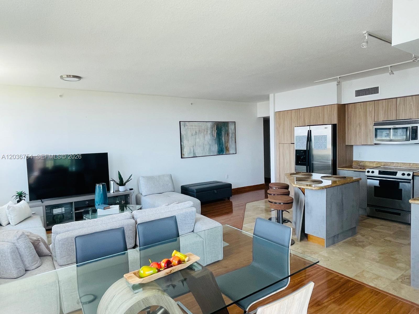 An open-concept living and dining area features a modern kitchen, glass table, and sectional sofa — HALLANDALE BEACH, FL