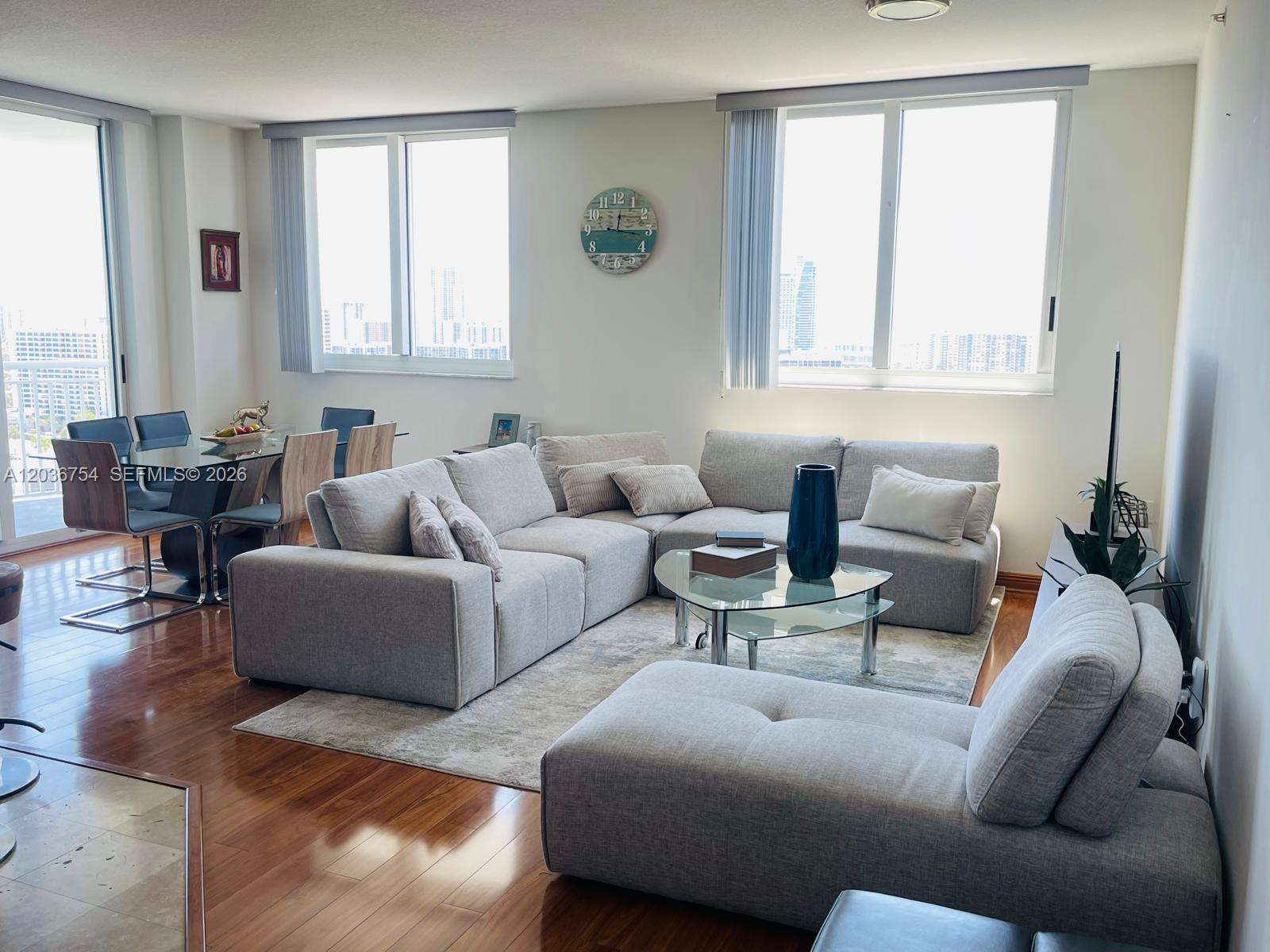A living room features a large gray sectional sofa, a glass coffee table, and city views — HALLANDALE BEACH, FL