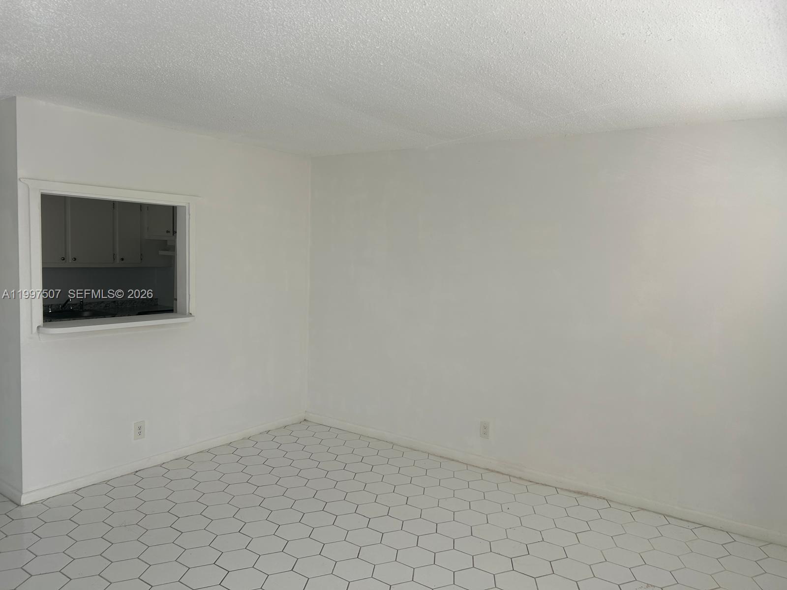 An empty room features white walls, a kitchen pass-through window, and white hexagonal floor tiles — 89 Berkshire D # 89, West Palm Beach FL 33417, WEST PALM BEACH, FL