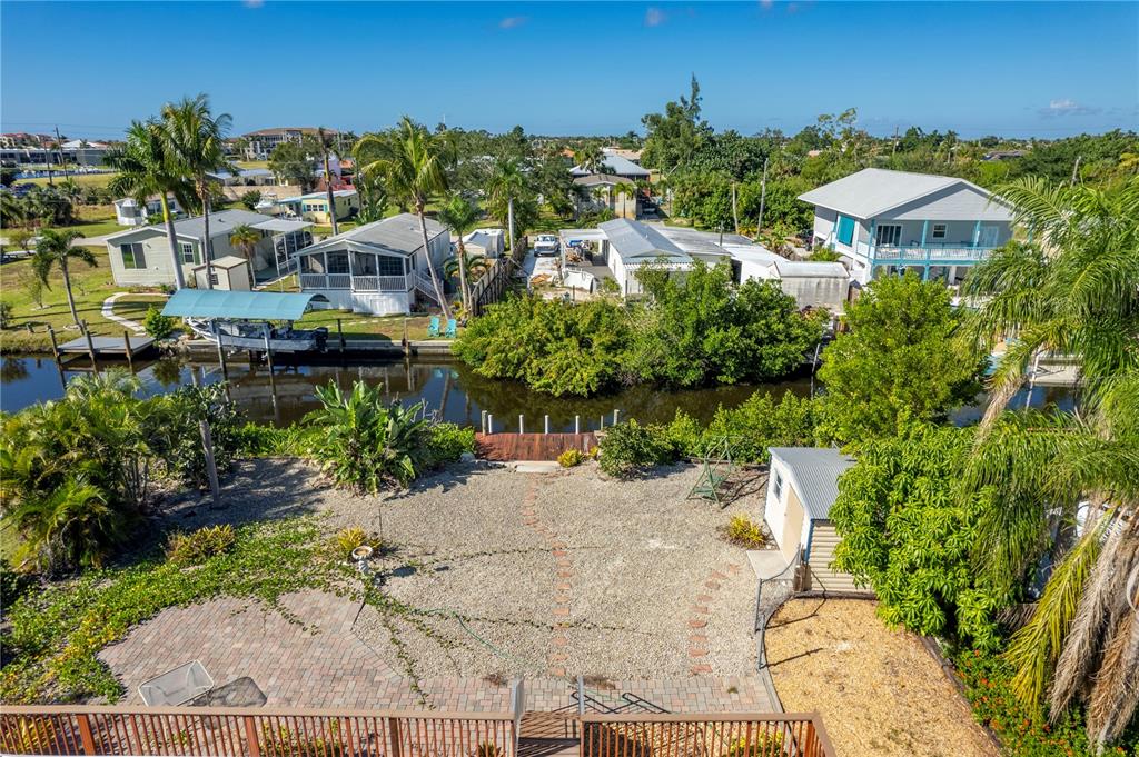 An elevated view of a backyard with a gravel area, patio, and canal access — 3101 BAMBOO COURT, PUNTA GORDA, FL