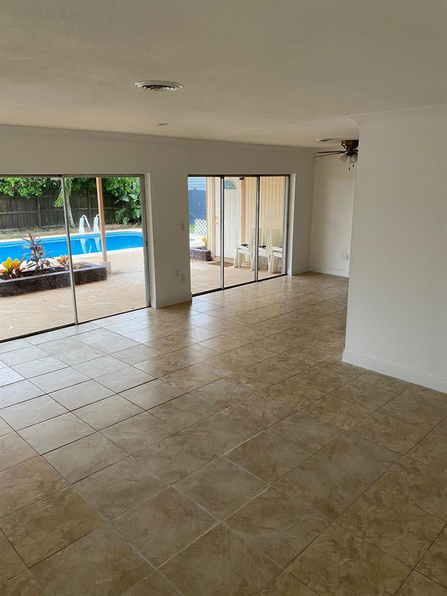 An interior room with beige tile flooring features two sliding glass doors overlooking a pool — 18 Andros Road, Palm Springs FL 33461, PALM SPRINGS, FL