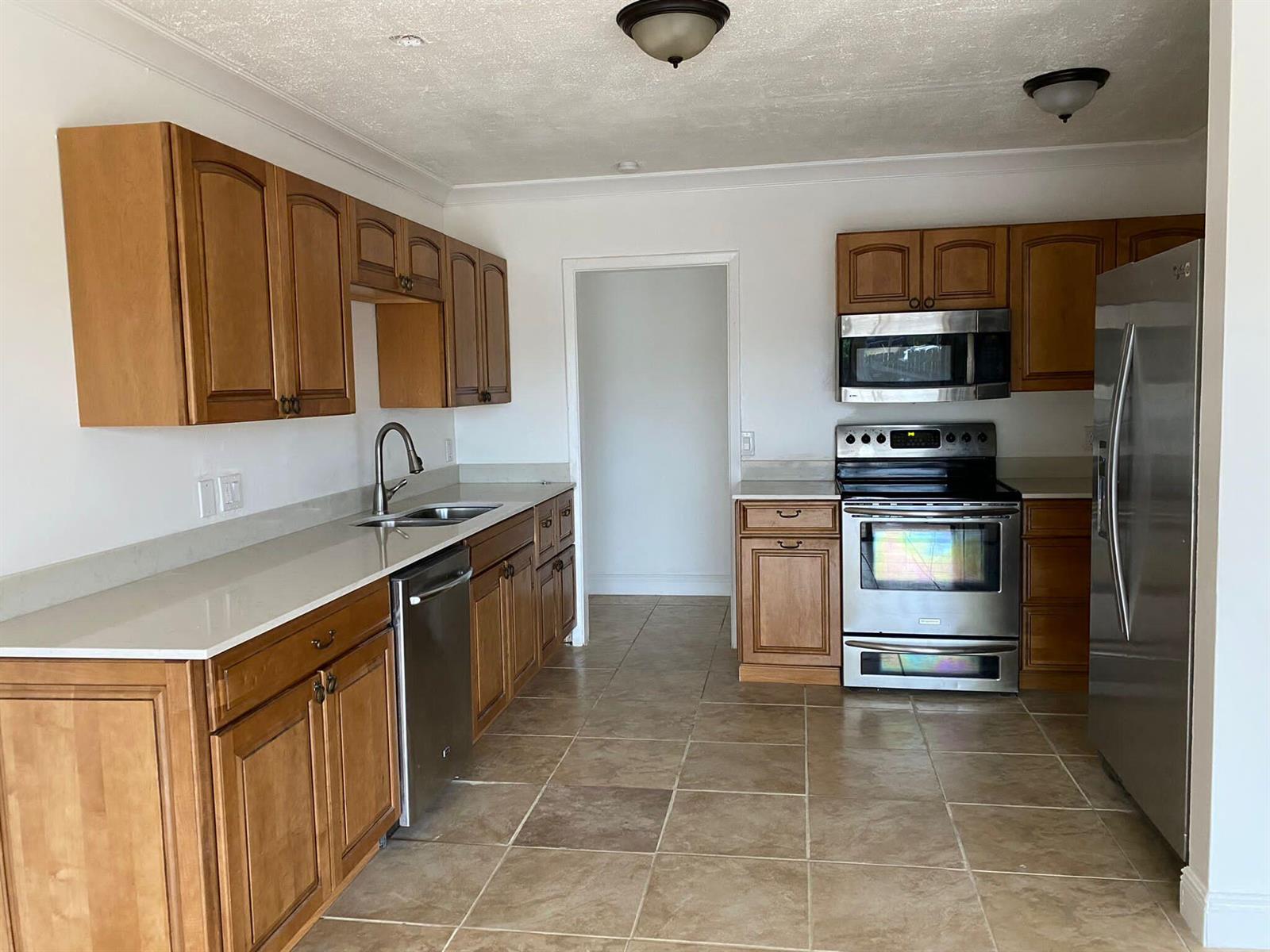 A kitchen features wood cabinets, stainless steel appliances, light countertops, and tan tile flooring — 18 Andros Road, Palm Springs FL 33461, PALM SPRINGS, FL