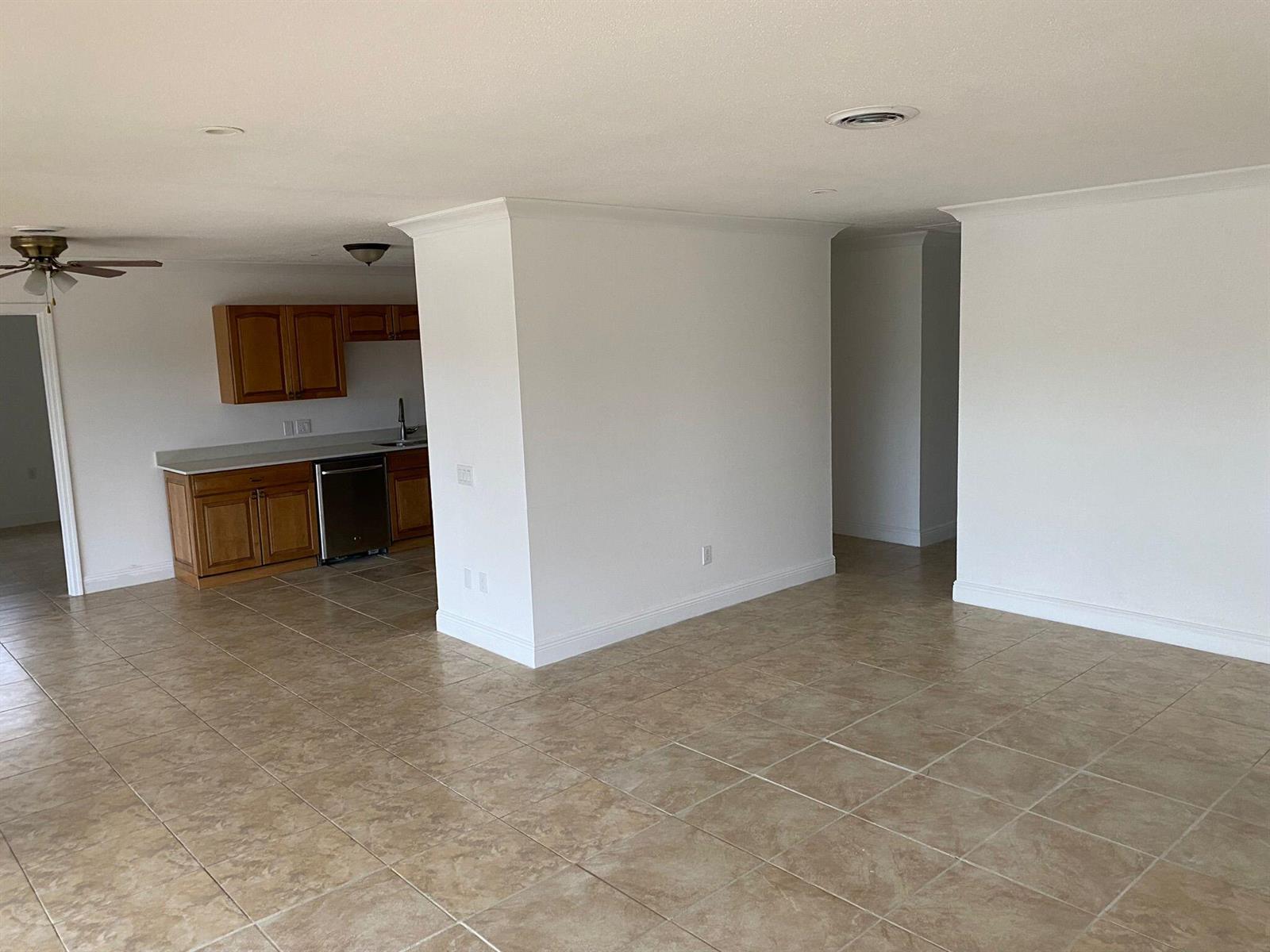 An open-concept living area features tile flooring, white walls, and a kitchen with wooden cabinets — 18 Andros Road, Palm Springs FL 33461, PALM SPRINGS, FL