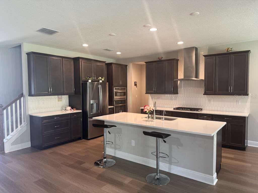 A kitchen with dark cabinetry, a white quartz island, stainless steel appliances, and wood flooring — 14698 HORSE TROT ROAD, LITHIA, FL