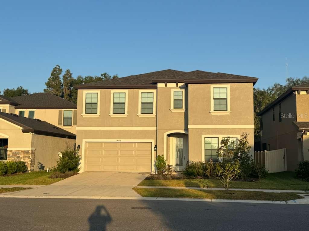 A two-story suburban house features a tan stucco exterior, a two-car garage, and a driveway — 14698 HORSE TROT ROAD, LITHIA, FL