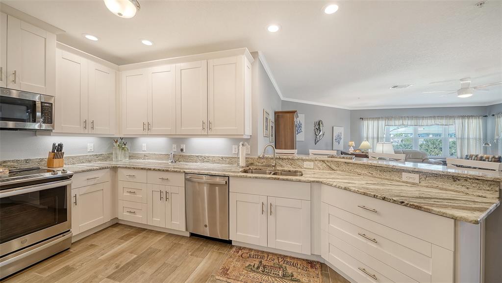 A kitchen features white cabinets, granite countertops, stainless steel appliances, and wood-look flooring — 7910 34TH AVENUE W UNIT 203, BRADENTON, FL
