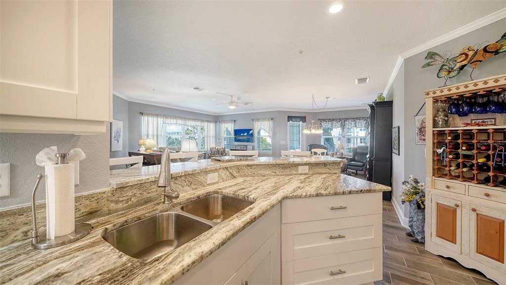 A kitchen with granite countertops and a double sink overlooks an open-concept living area — 7910 34TH AVENUE W UNIT 203, BRADENTON, FL