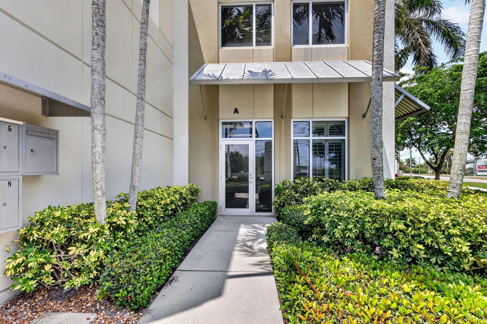 A concrete walkway leads to the glass entrance door of a tan commercial building labeled A — 1250 Wallace Drive # A, Delray Beach FL 33444, DELRAY BEACH, FL