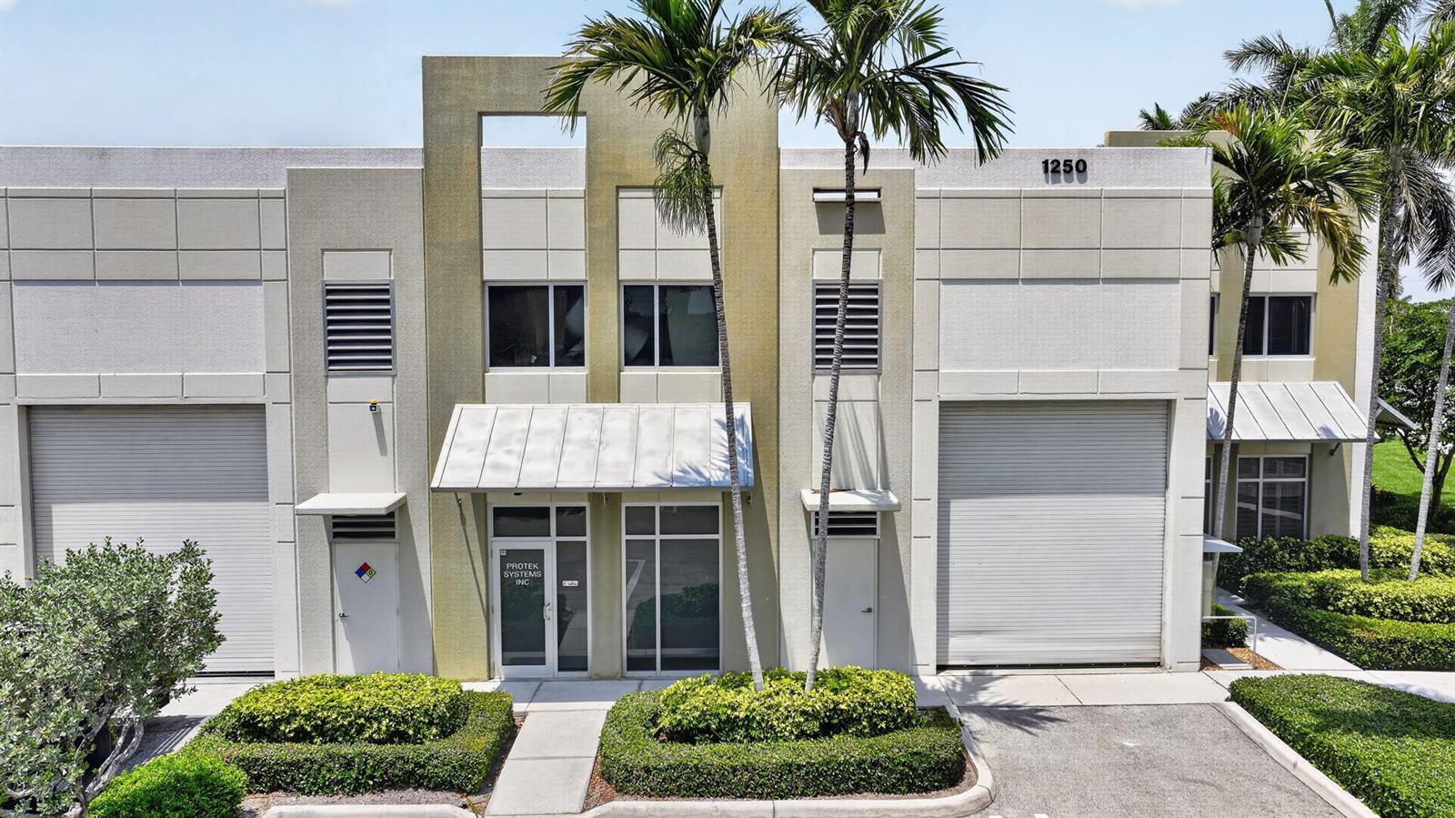 An exterior view of a two-story commercial building with roll-up doors and palm trees — 1250 Wallace Drive # A, Delray Beach FL 33444, DELRAY BEACH, FL