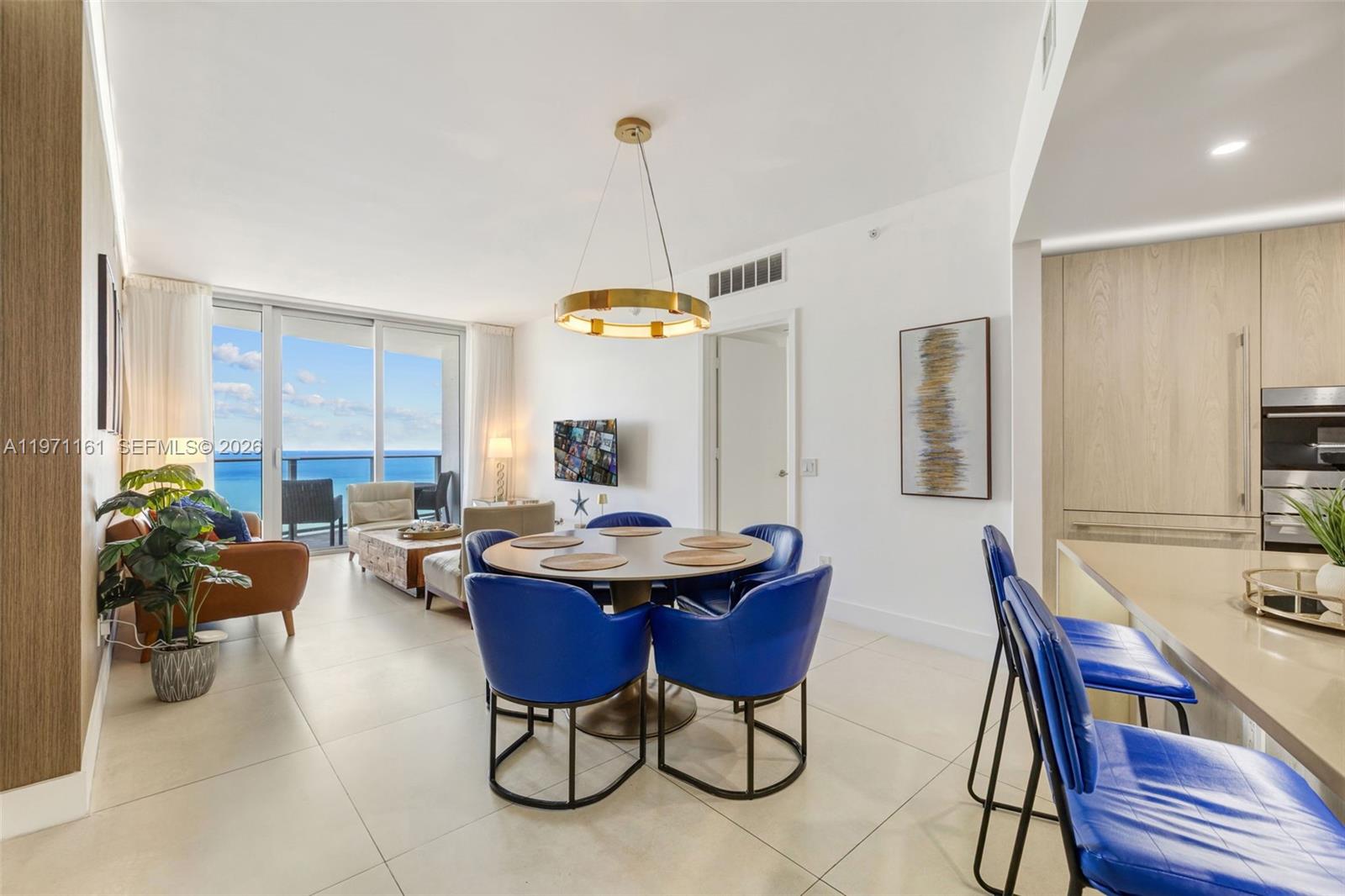 A modern dining and living area features blue chairs, a gold chandelier, and ocean views — 4111 S Ocean Dr # 3706, Hollywood FL 33019, HOLLYWOOD, FL