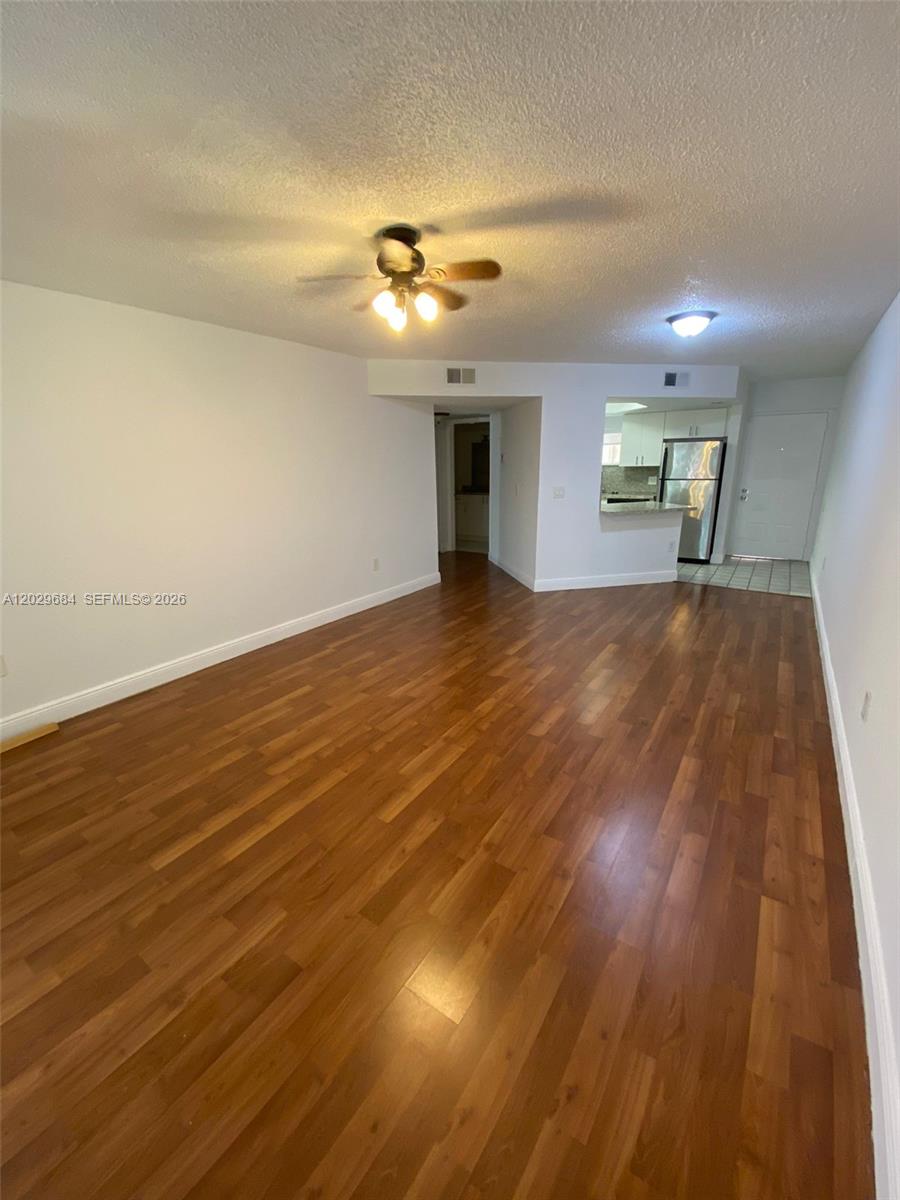 An empty living room features wood-look flooring, a ceiling fan, and an adjacent kitchen area — 8323 Lake Dr # 302, Doral FL 33166, DORAL, FL