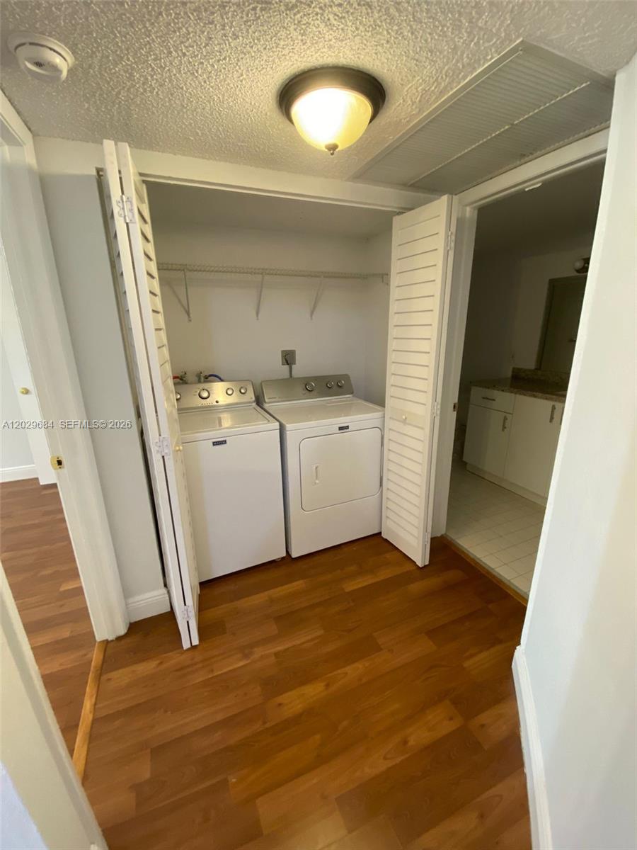 A laundry closet with a washer and dryer sits between two doorways on wood flooring — 8323 Lake Dr # 302, Doral FL 33166, DORAL, FL