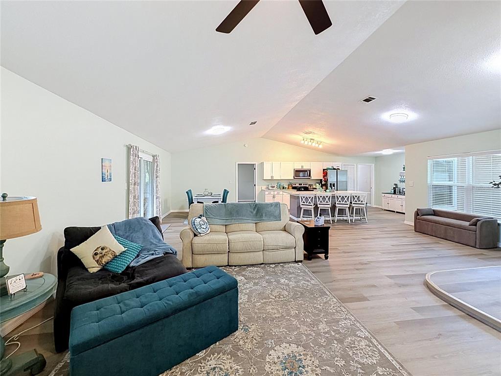 An open-concept living room and kitchen feature light wood-look flooring and vaulted ceilings — 706 OLD CREEK COURT, SANFORD, FL