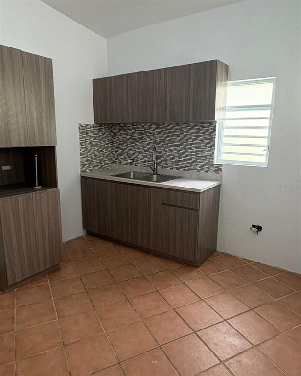 A kitchen features wood-grain cabinets, a tiled backsplash, a stainless steel sink, and terracotta flooring — LA BARRA 105 F, CAGUAS, PR