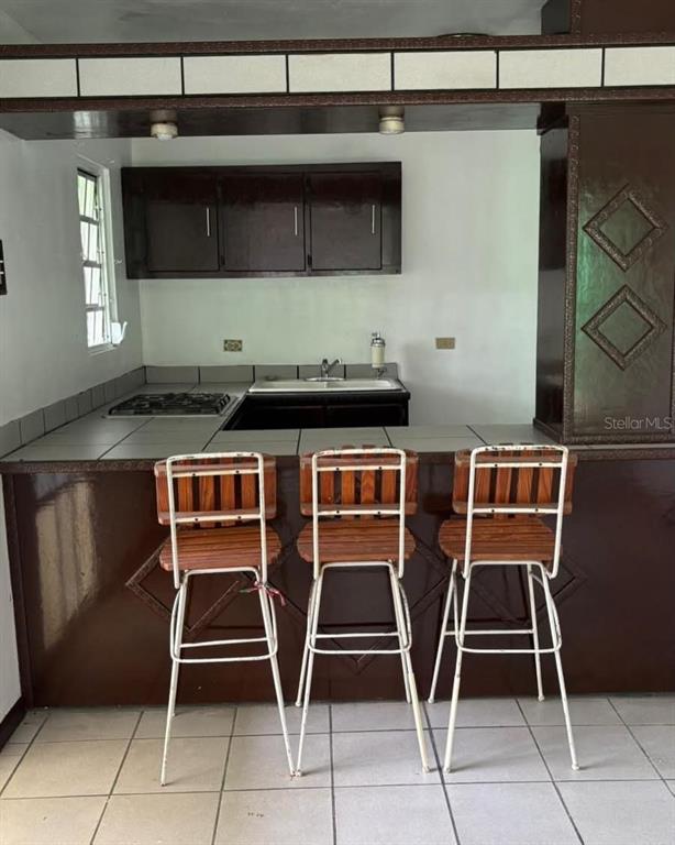 A kitchen features a breakfast bar with three wooden stools, dark cabinetry, and tiled countertops — LA BARRA 105 F, CAGUAS, PR