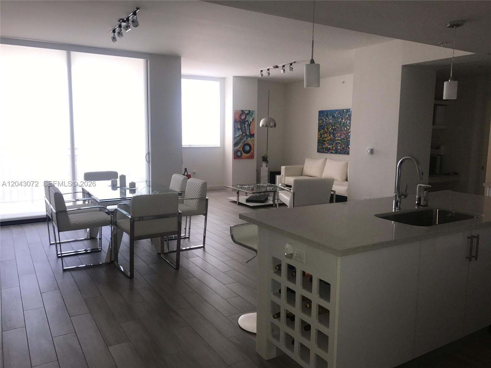 A modern open-concept living and dining area features white furniture, tile flooring, and a kitchen island — 999 SW 1st Ave # 2806, Miami FL 33130, MIAMI, FL