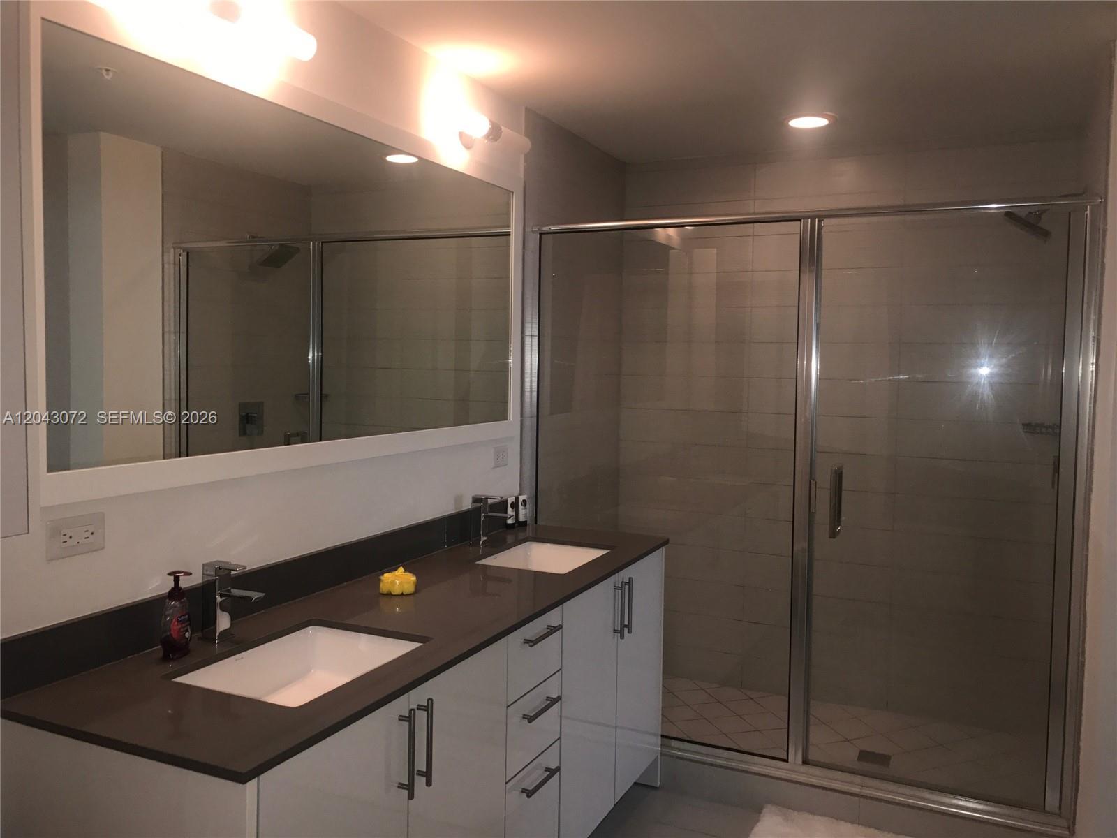 A modern bathroom features a double vanity with white cabinets, dark countertops, and a glass-enclosed shower — 999 SW 1st Ave # 2806, Miami FL 33130, MIAMI, FL