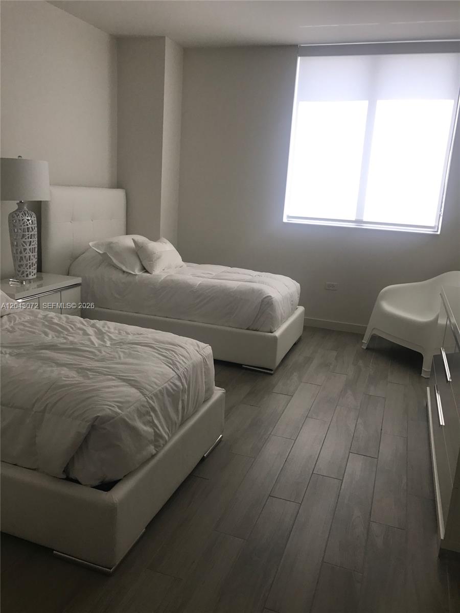 A bedroom features two white beds, a white chair, and gray wood-look flooring — 999 SW 1st Ave # 2806, Miami FL 33130, MIAMI, FL