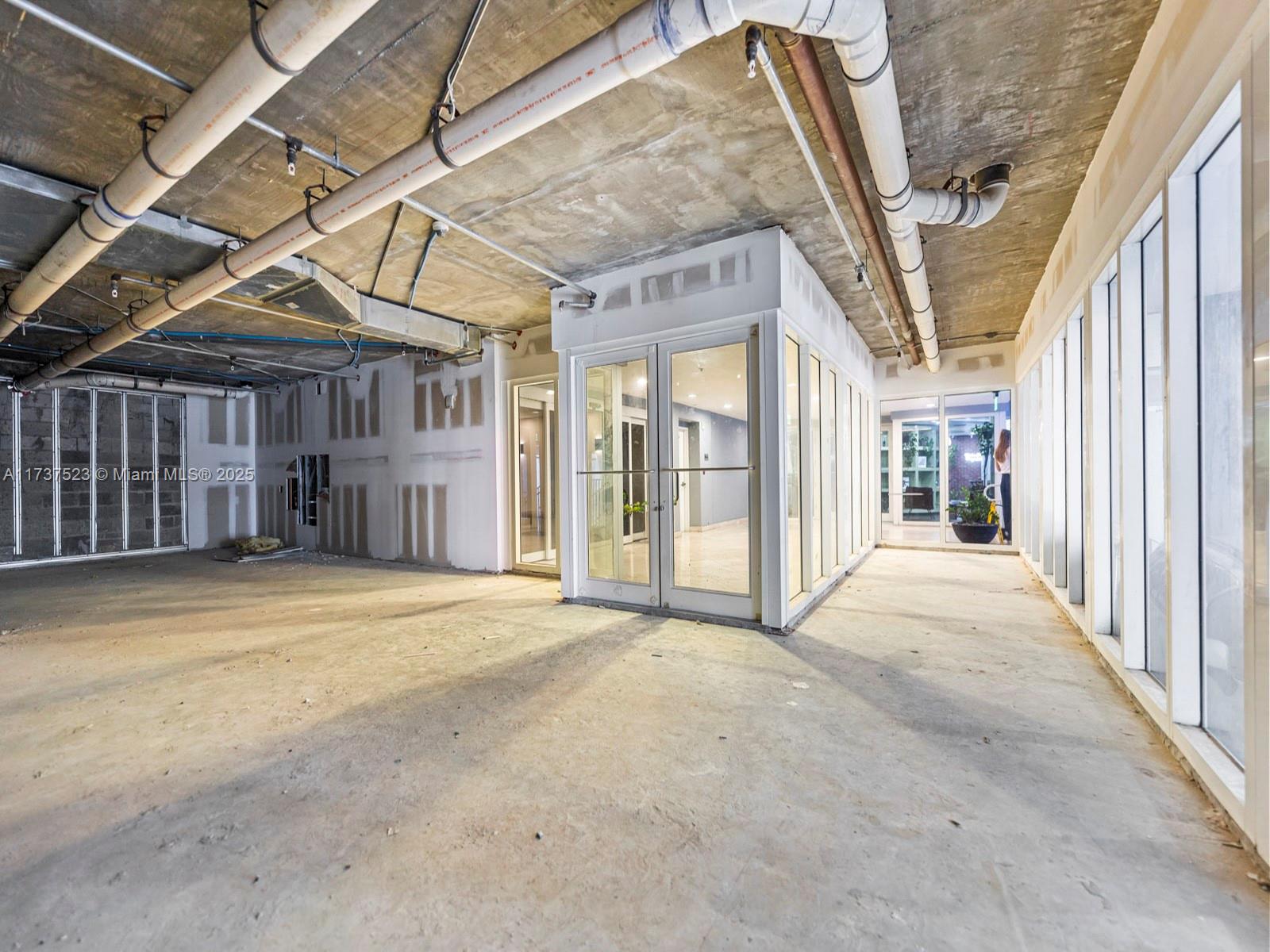 An unfinished commercial interior features exposed concrete ceilings, industrial piping, and a glass-enclosed office space — 170 SE 14th St, Miami FL 33131, MIAMI, FL