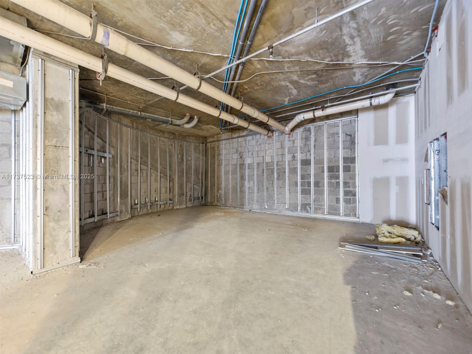 An unfinished room features exposed concrete walls, metal wall studs, and overhead plumbing pipes — 170 SE 14th St, Miami FL 33131, MIAMI, FL