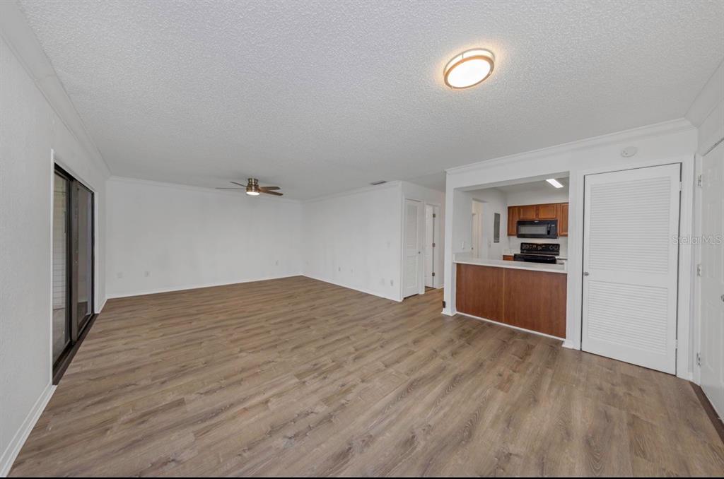 An empty living room with wood-look flooring, a ceiling fan, and an open kitchen pass-through — 643 HAVEN PLACE UNIT 643, TARPON SPRINGS, FL