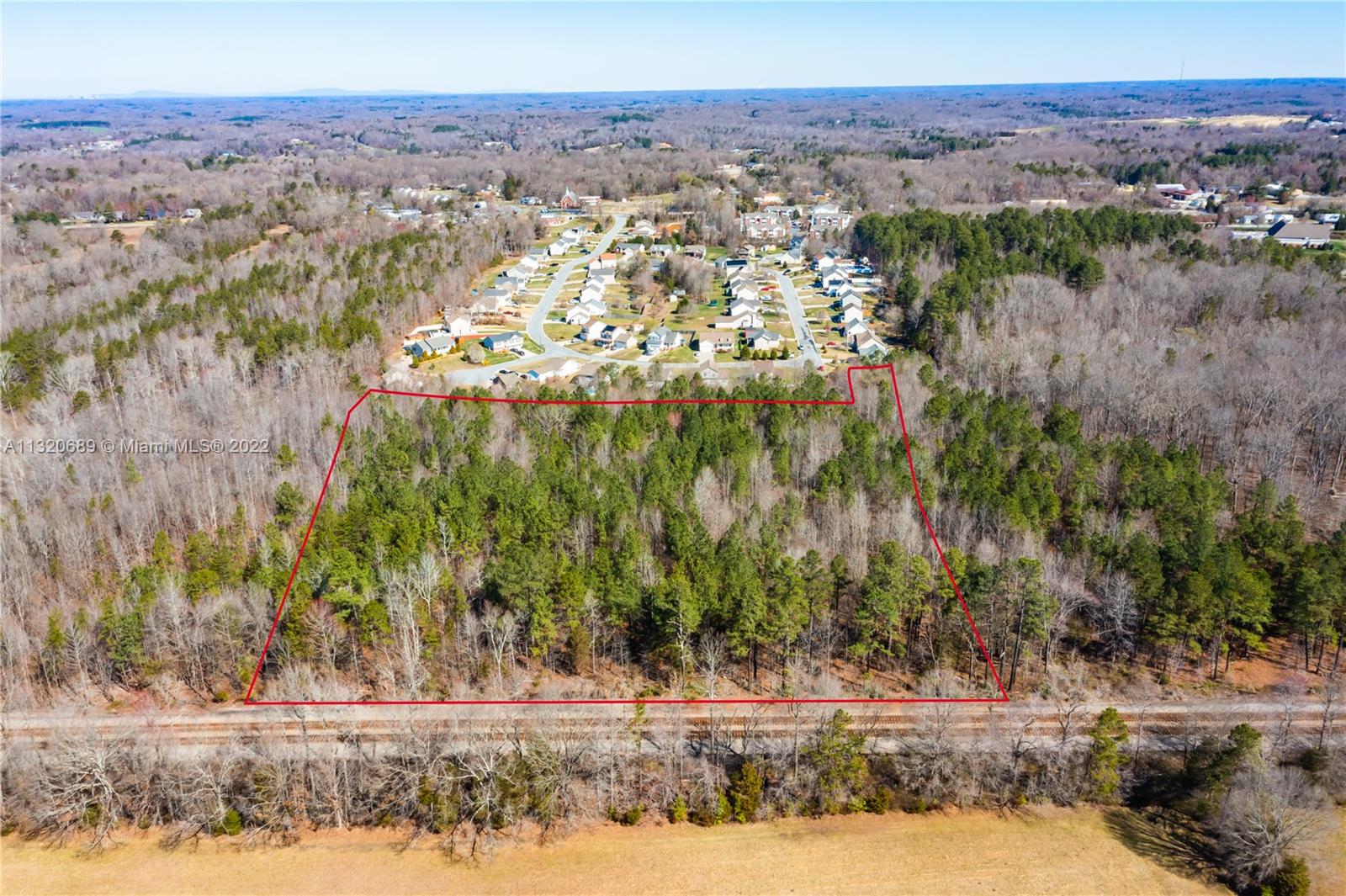 An aerial view shows a wooded lot outlined in red adjacent to a railroad track — 0 Coral Lane, NC 27360, NC