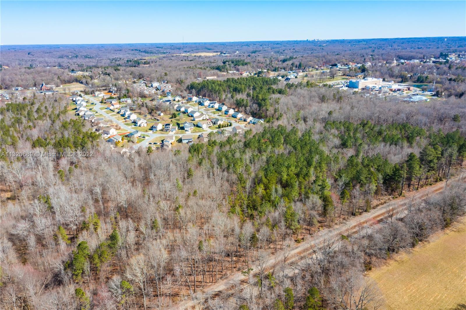 An aerial view shows a residential neighborhood bordering a large wooded area and open fields — 0 Coral Lane, NC 27360, NC