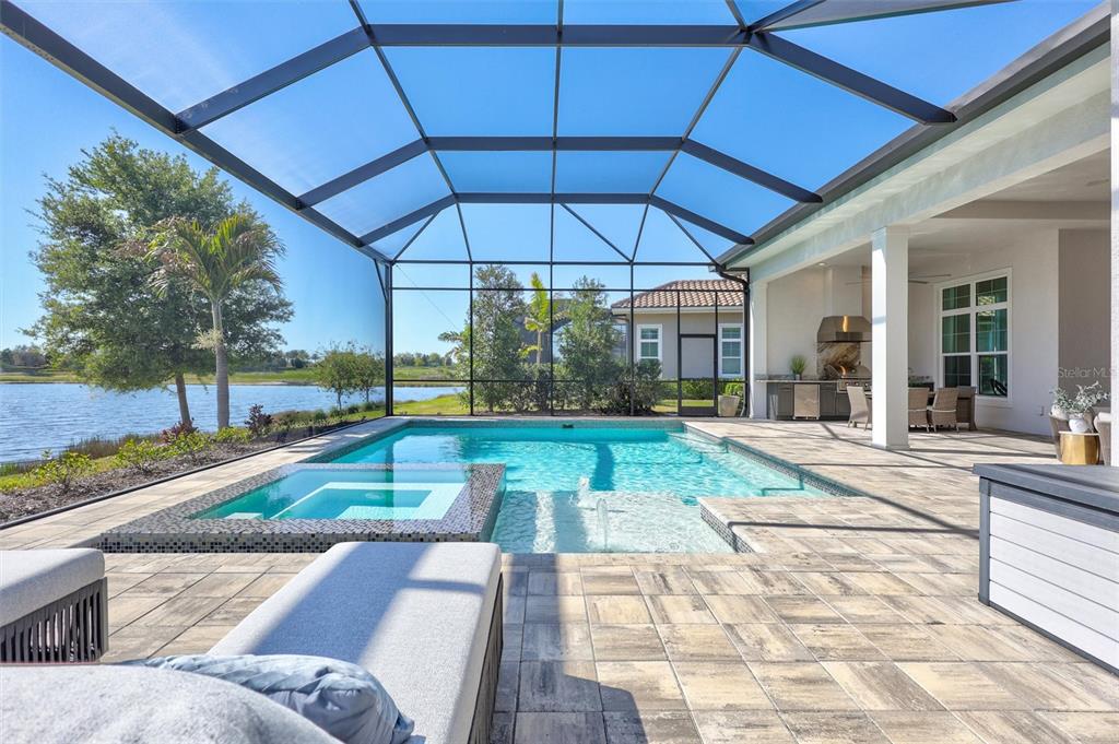 A screened-in patio features a swimming pool, a raised spa, and an outdoor kitchen area — 8278 PAVIA WAY, BRADENTON, FL