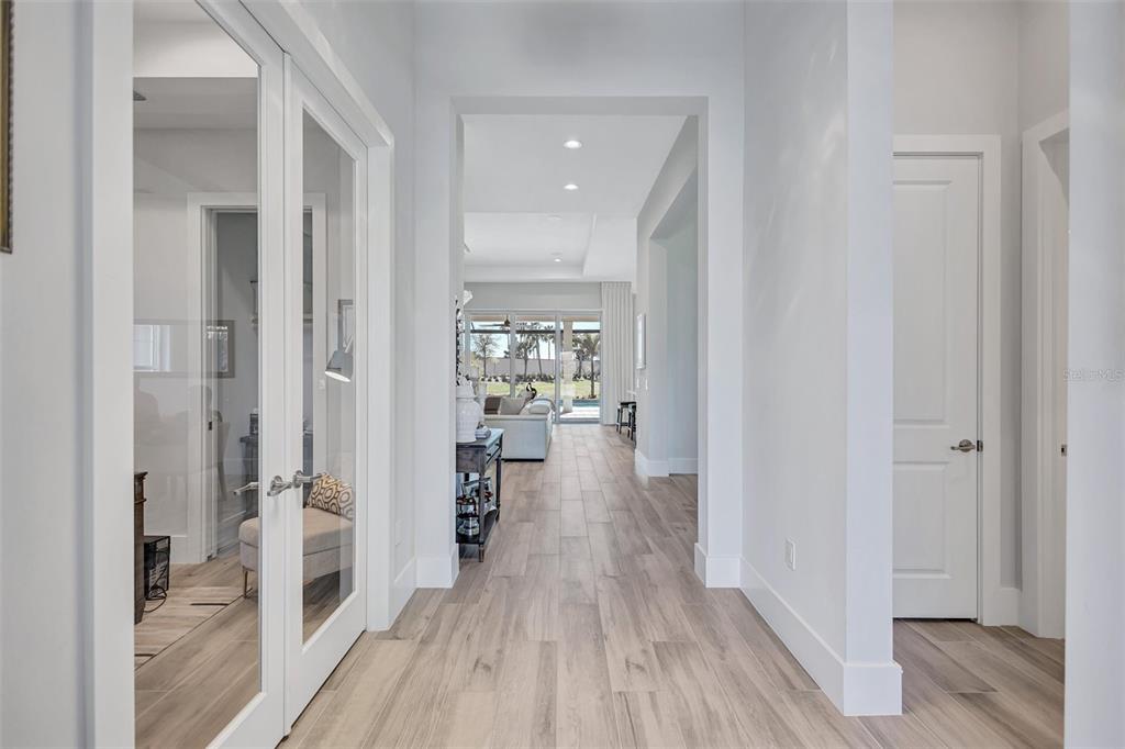 A bright hallway with light wood-look tile flooring leads to an open living area — 8278 PAVIA WAY, BRADENTON, FL