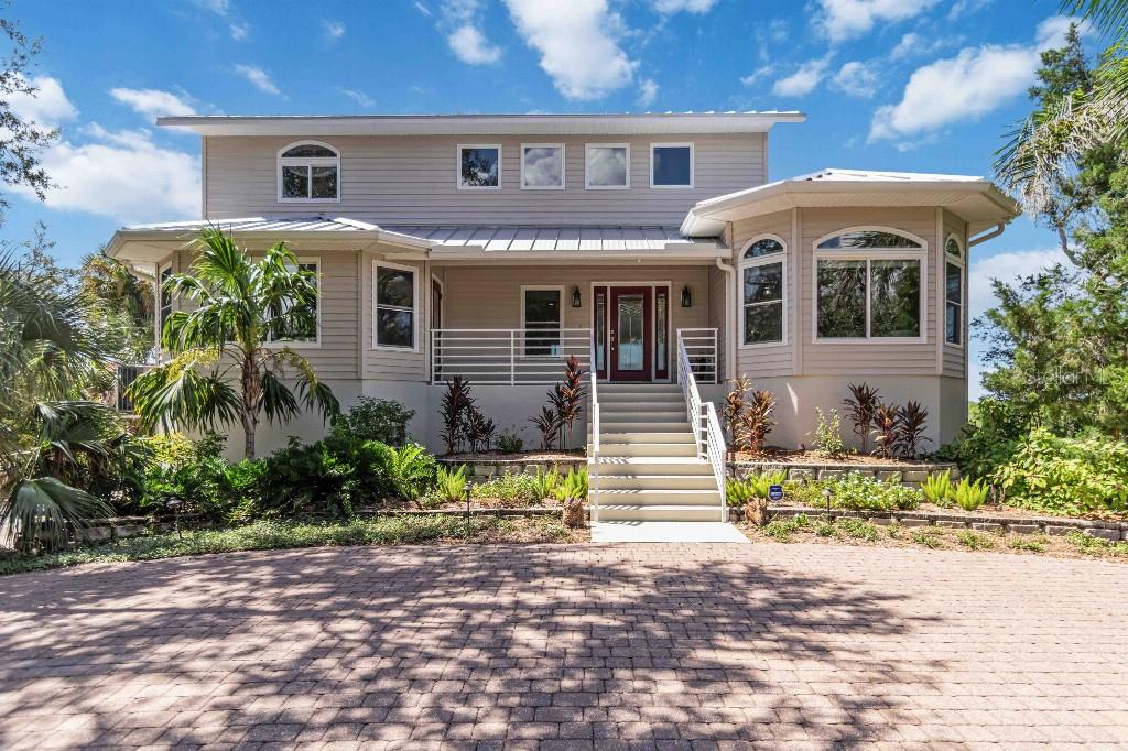 A three-story house with screened balconies sits behind a large grassy yard with a firepit — 6511 BAYSHORE ROAD, PALMETTO, FL