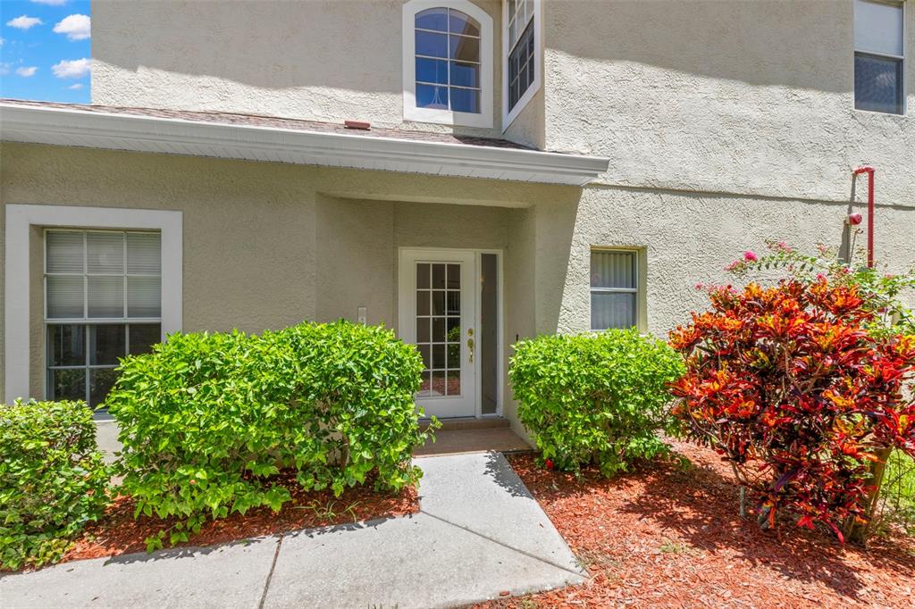 The exterior of a two-story building features a white front door, windows, and landscaping — 11117 KAPOK GRAND CIRCLE, MADEIRA BEACH, FL