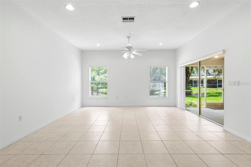 A bright, empty living room with white walls, tile flooring, a ceiling fan, and sliding doors — 11117 KAPOK GRAND CIRCLE, MADEIRA BEACH, FL