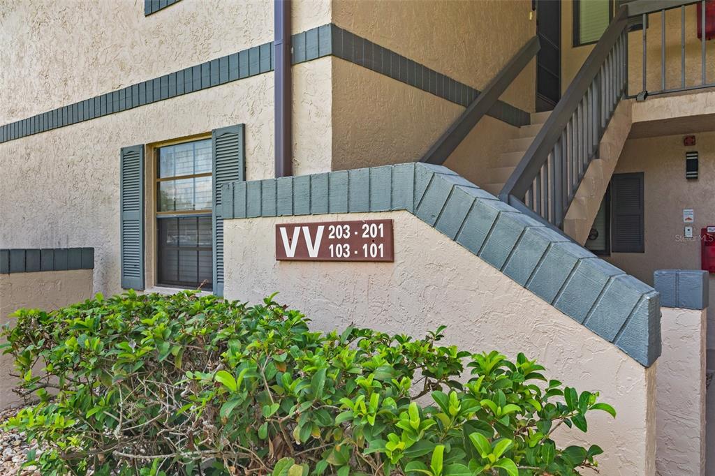 An exterior view of a tan apartment building with a staircase and unit number sign — 19505 QUESADA AVENUE UNIT VV201, PORT CHARLOTTE, FL