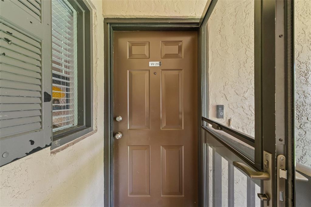 A brown front door with a screen door and a window with shutters — 19505 QUESADA AVENUE UNIT VV201, PORT CHARLOTTE, FL
