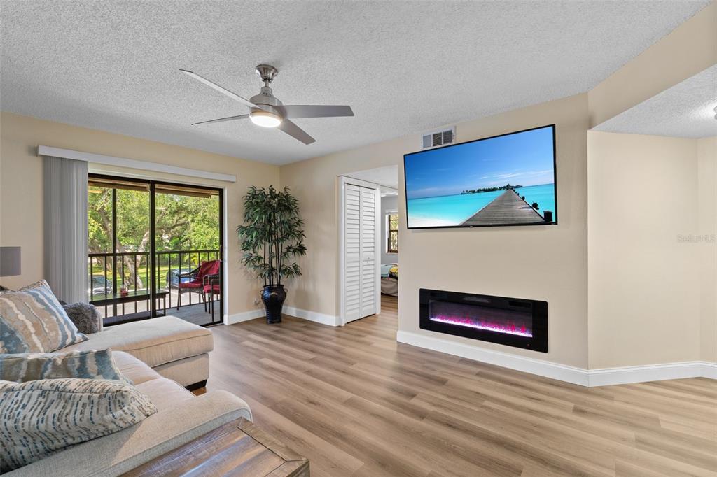 A living room features wood-look flooring, a ceiling fan, a wall-mounted television, and an electric fireplace — 19505 QUESADA AVENUE UNIT VV201, PORT CHARLOTTE, FL