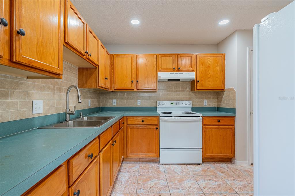 A kitchen features wood cabinets, green countertops, a white stove, and a tiled backsplash — 746-748 MINK CT, POINCIANA, FL