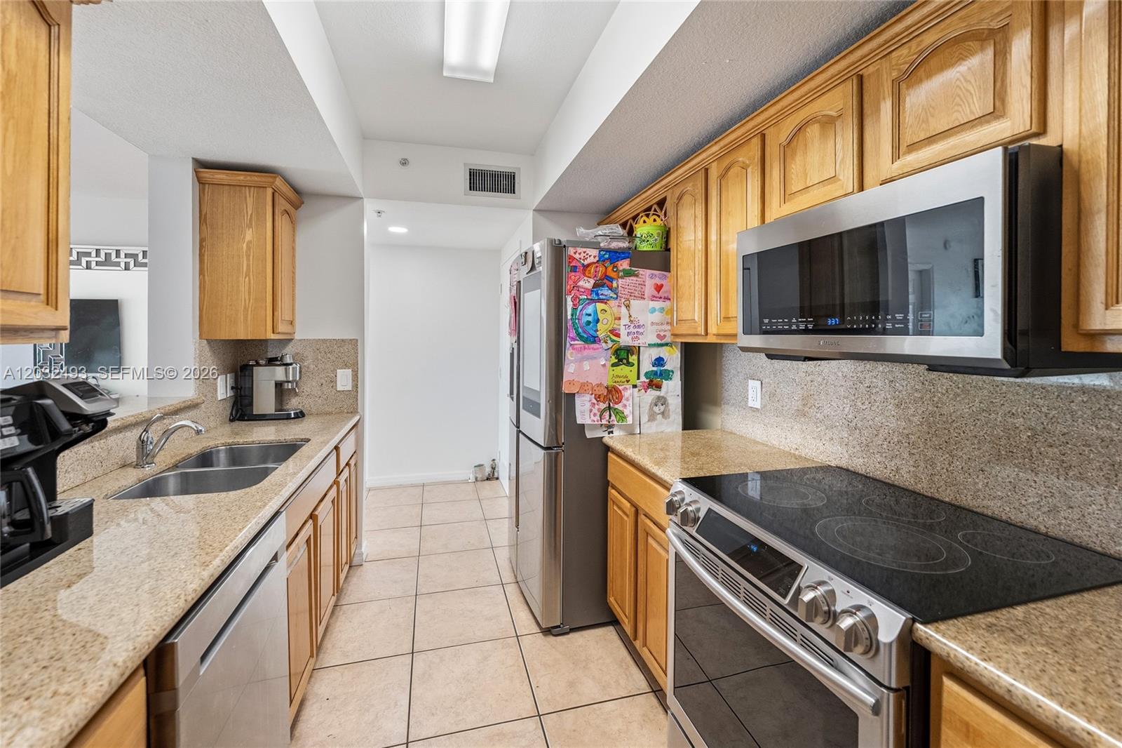 A galley kitchen features light wood cabinets, granite countertops, and stainless steel appliances — 4242 NW 2nd St # 1001, Miami FL 33126, MIAMI, FL