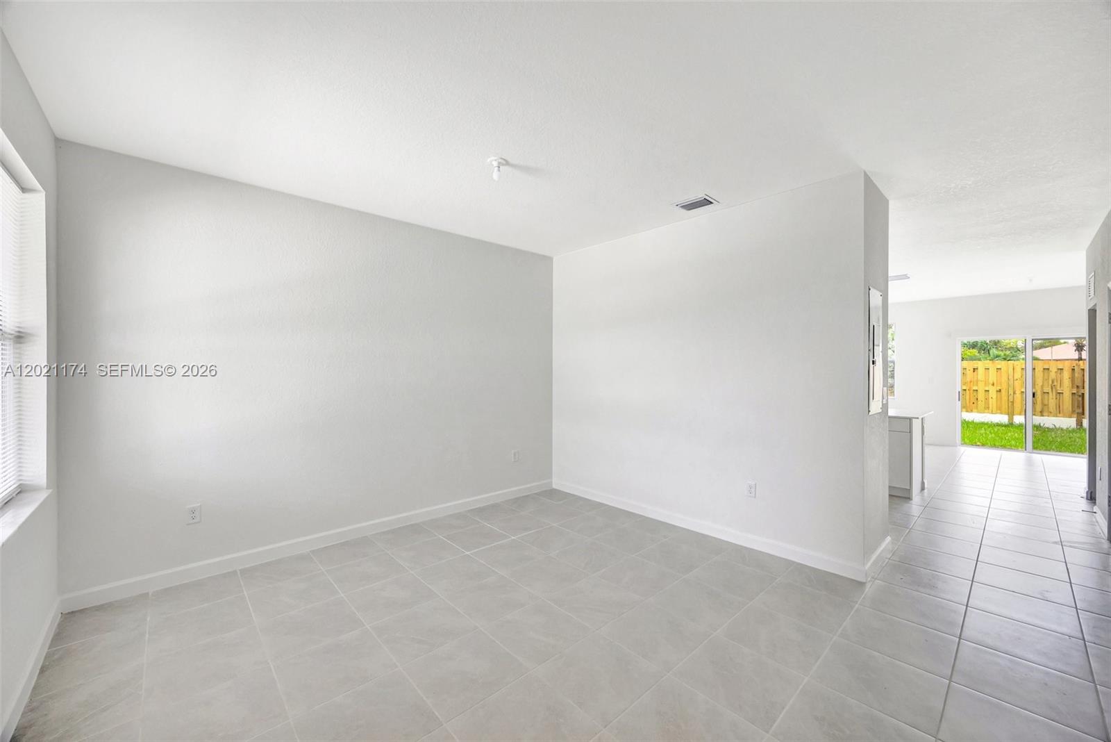 An empty room with light-colored tile flooring and white walls leads to a sliding glass door — HOMESTEAD, FL