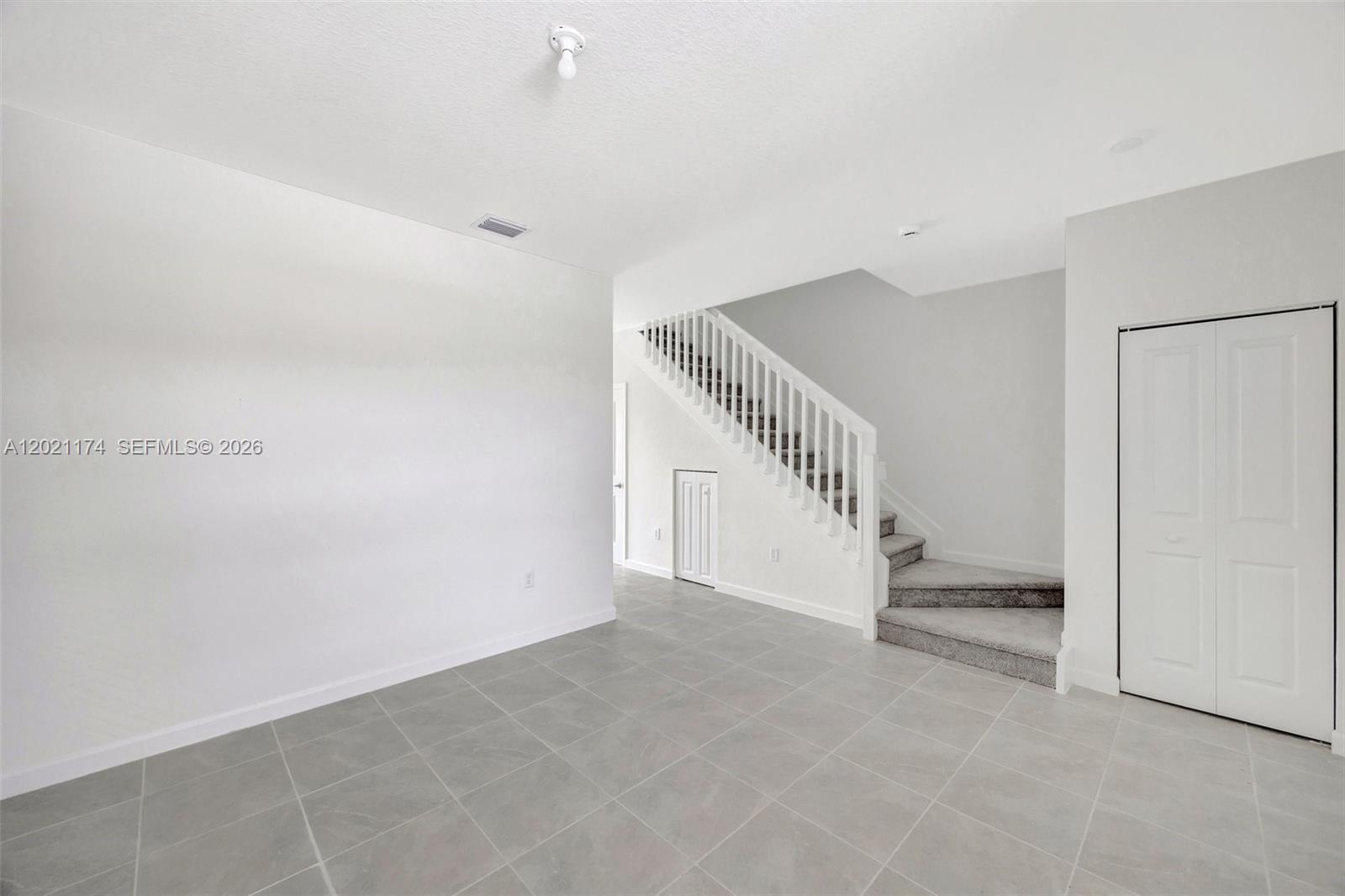 An empty room features gray tile flooring, white walls, and a staircase with carpeted steps — HOMESTEAD, FL
