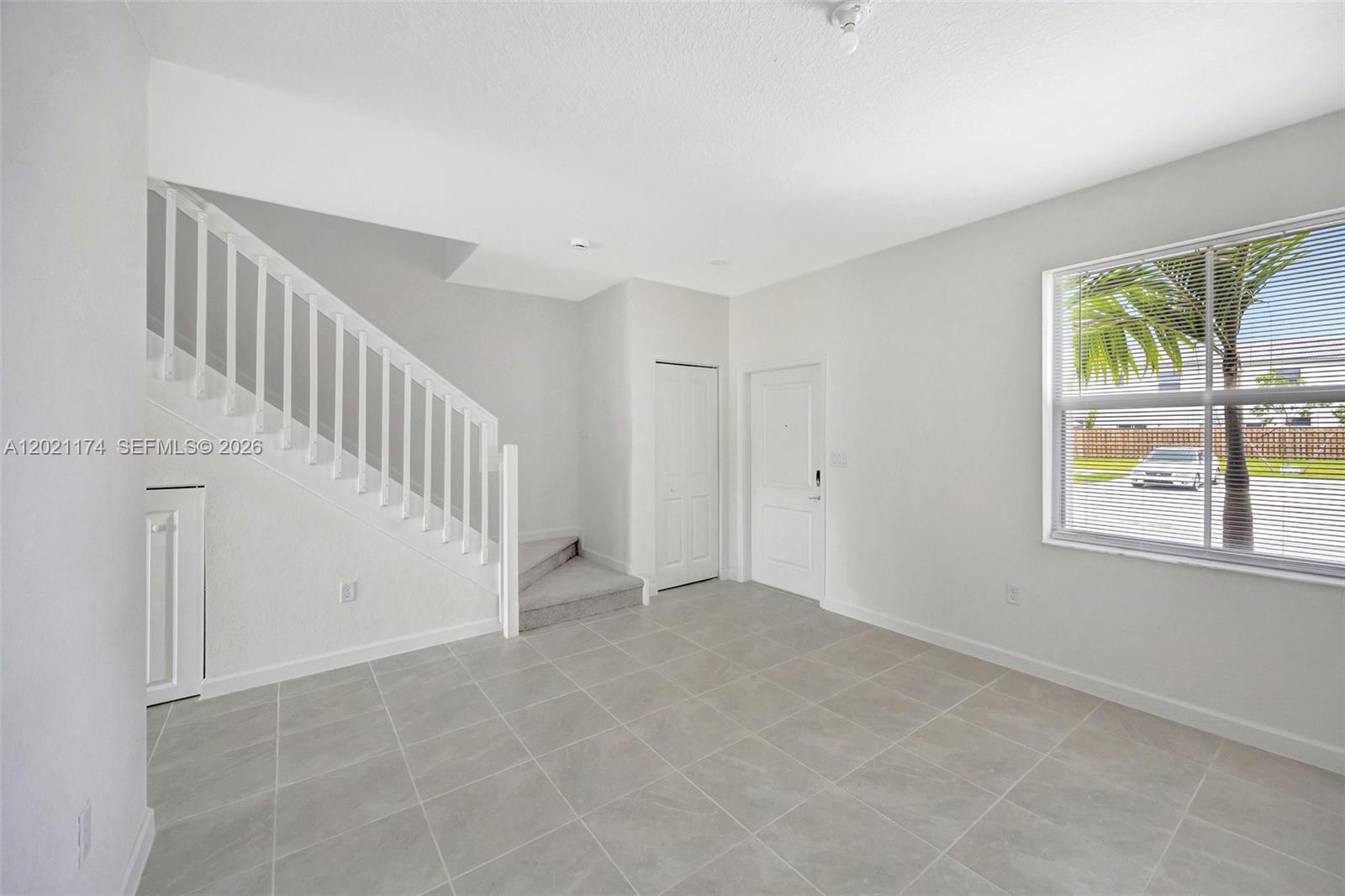 A room with light gray tile flooring, a white staircase, and a window with blinds — HOMESTEAD, FL