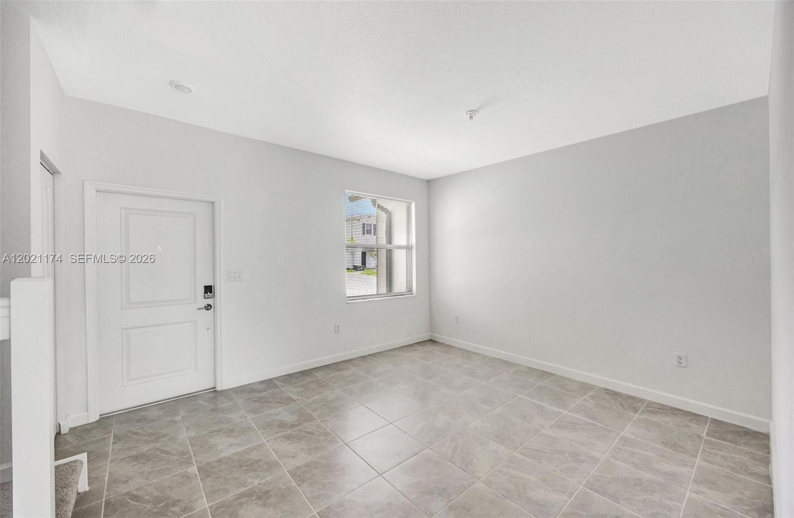 An empty room features light gray walls, large square floor tiles, and a white door — HOMESTEAD, FL