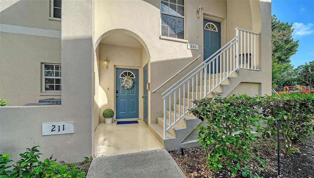 The exterior of a two-story building features two blue front doors and white railings — 8375 GLENROSE WAY UNIT 211, SARASOTA, FL
