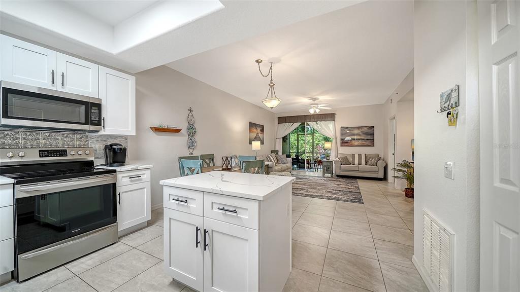 A modern kitchen with white cabinets and a quartz island opens into a living area — 8375 GLENROSE WAY UNIT 211, SARASOTA, FL