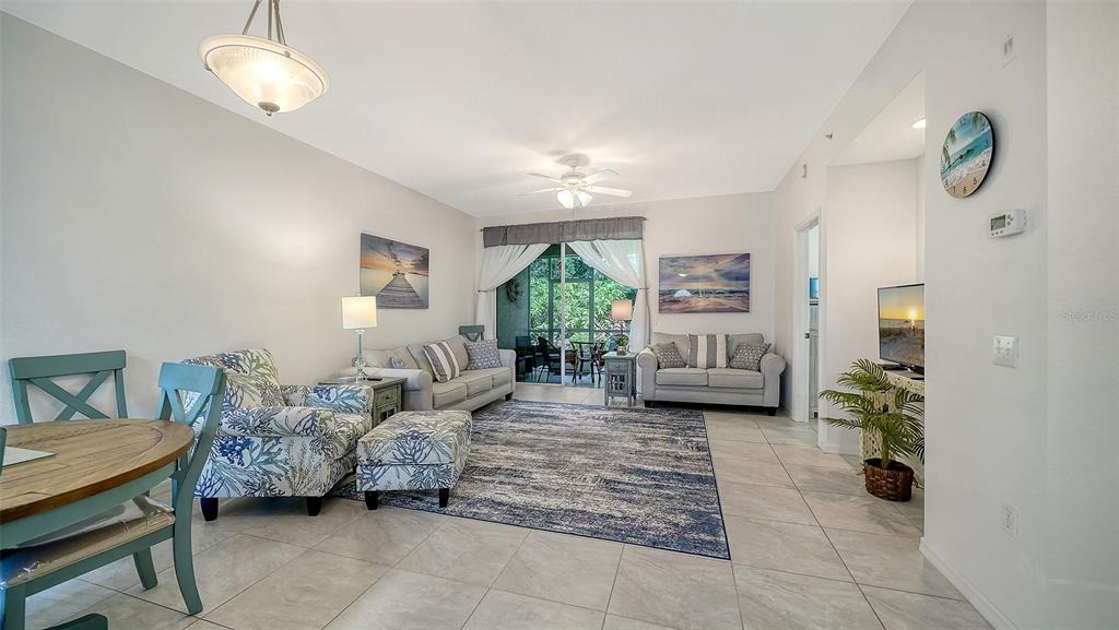 A living room with tile floors, a large area rug, and a sliding door to a balcony — 8375 GLENROSE WAY UNIT 211, SARASOTA, FL