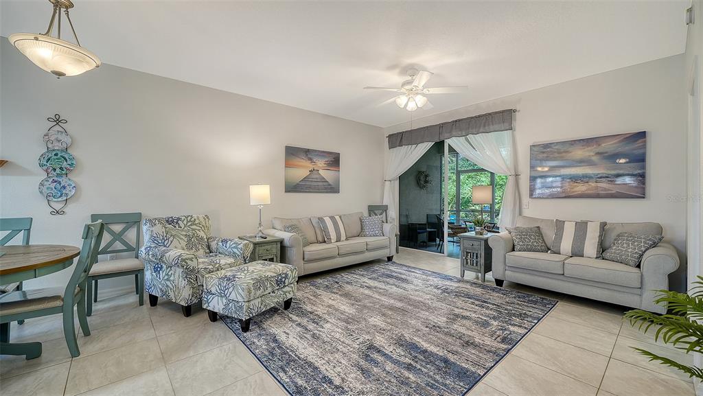 A living room features two beige sofas, a patterned armchair with ottoman, and tile flooring — 8375 GLENROSE WAY UNIT 211, SARASOTA, FL