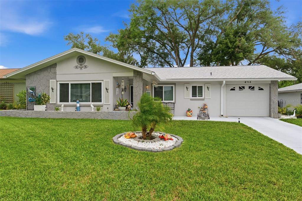 A single-story house with a gray stone facade, a white garage, and a front lawn — 8715 BENTON DRIVE, PORT RICHEY, FL