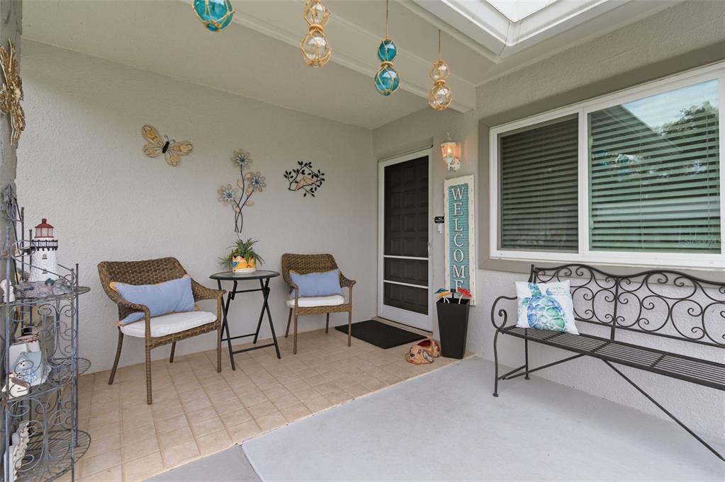 A covered porch features wicker chairs, a metal bench, and coastal-themed wall decor — 8715 BENTON DRIVE, PORT RICHEY, FL