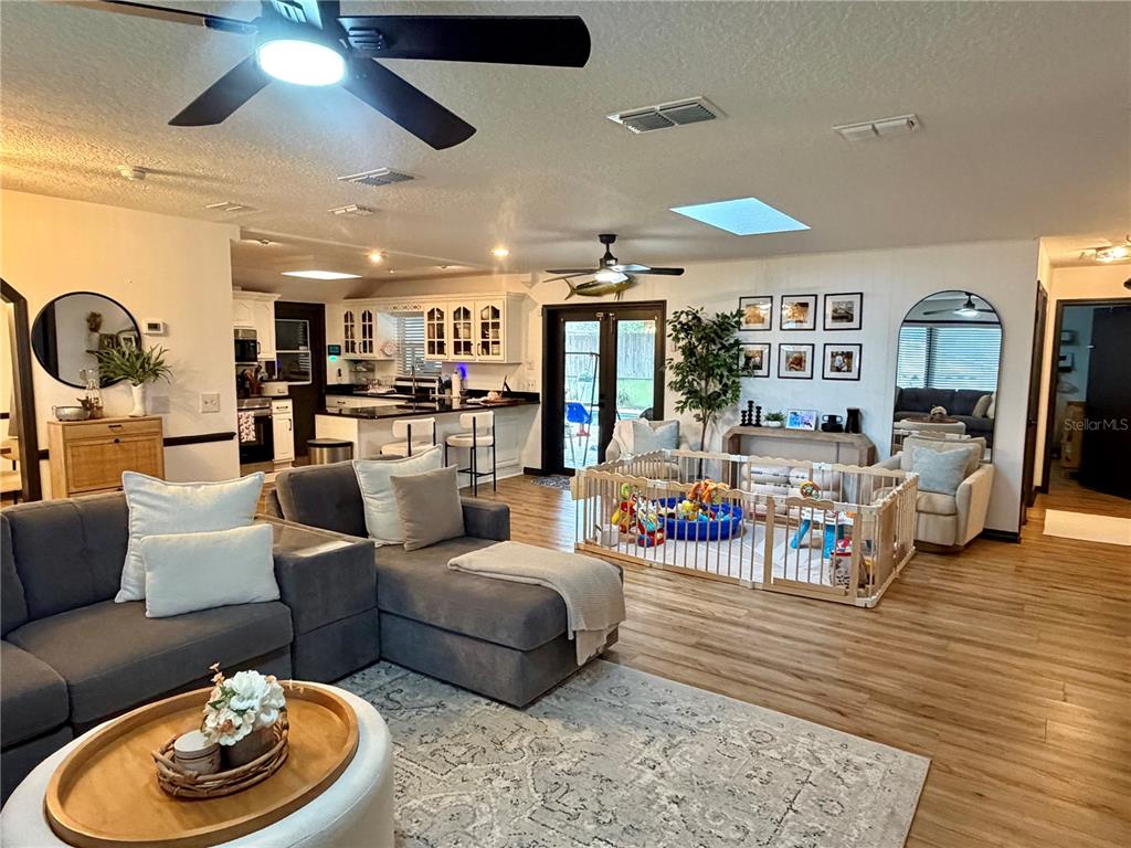 A living room with a sectional sofa, kitchen, and a child's playpen on wood flooring — 1105 DORIS STREET, ALTAMONTE SPRINGS, FL
