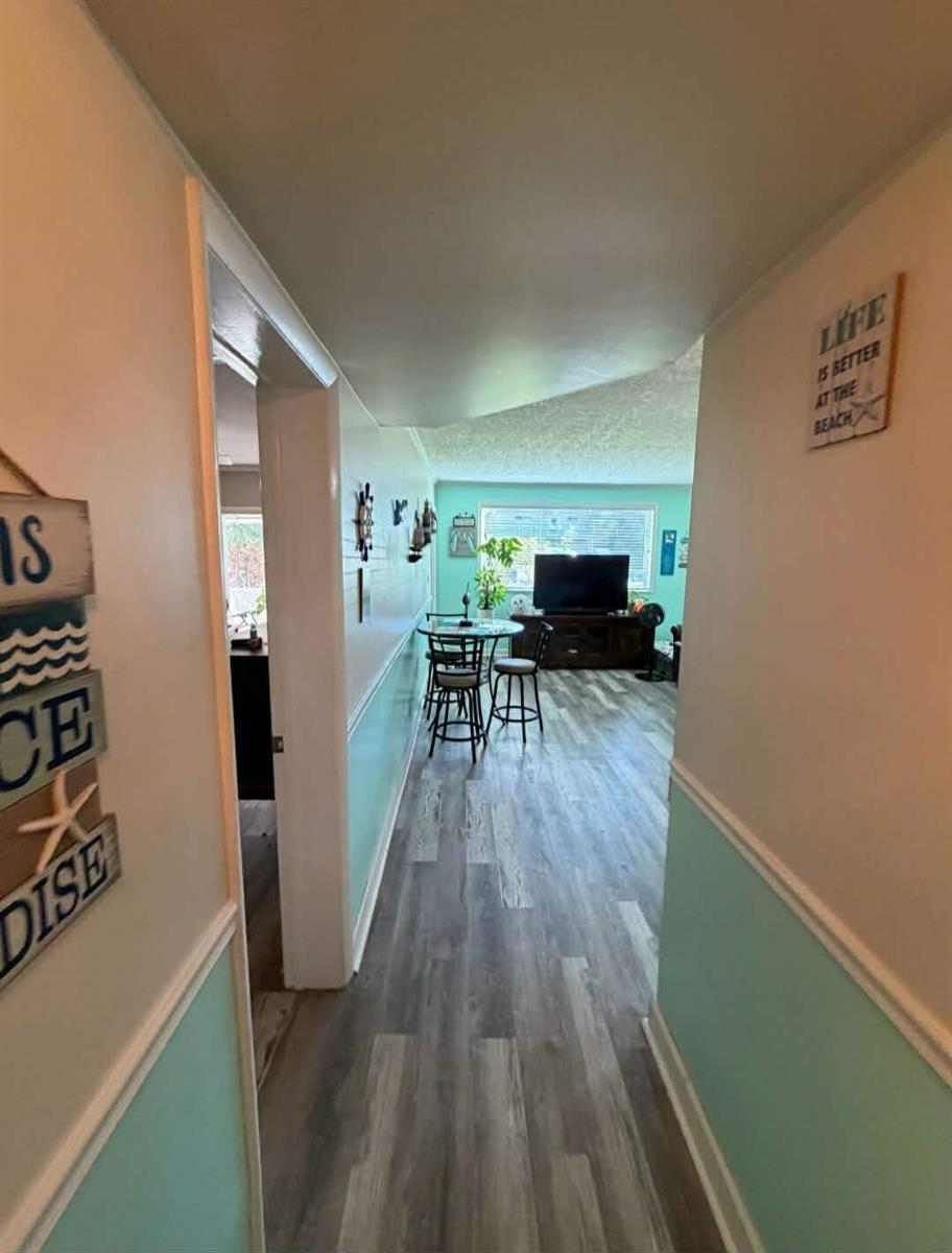 A hallway with light blue walls and wood-look flooring leads into a living area — 2770 S Garden Drive # 107, FL 33461, FL